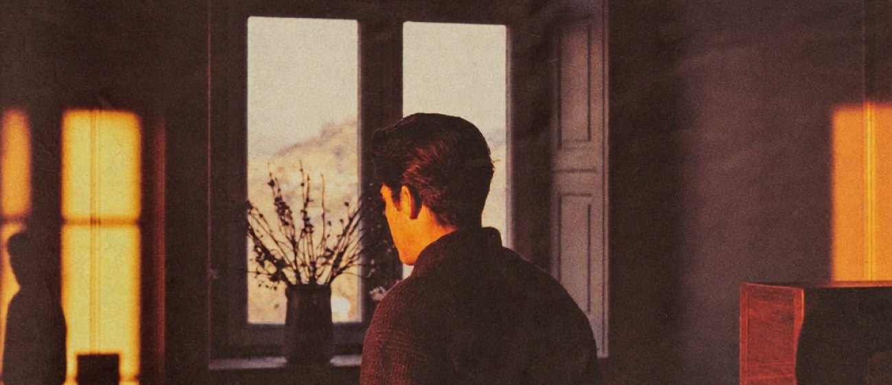 Man looking out a window in warm evening light