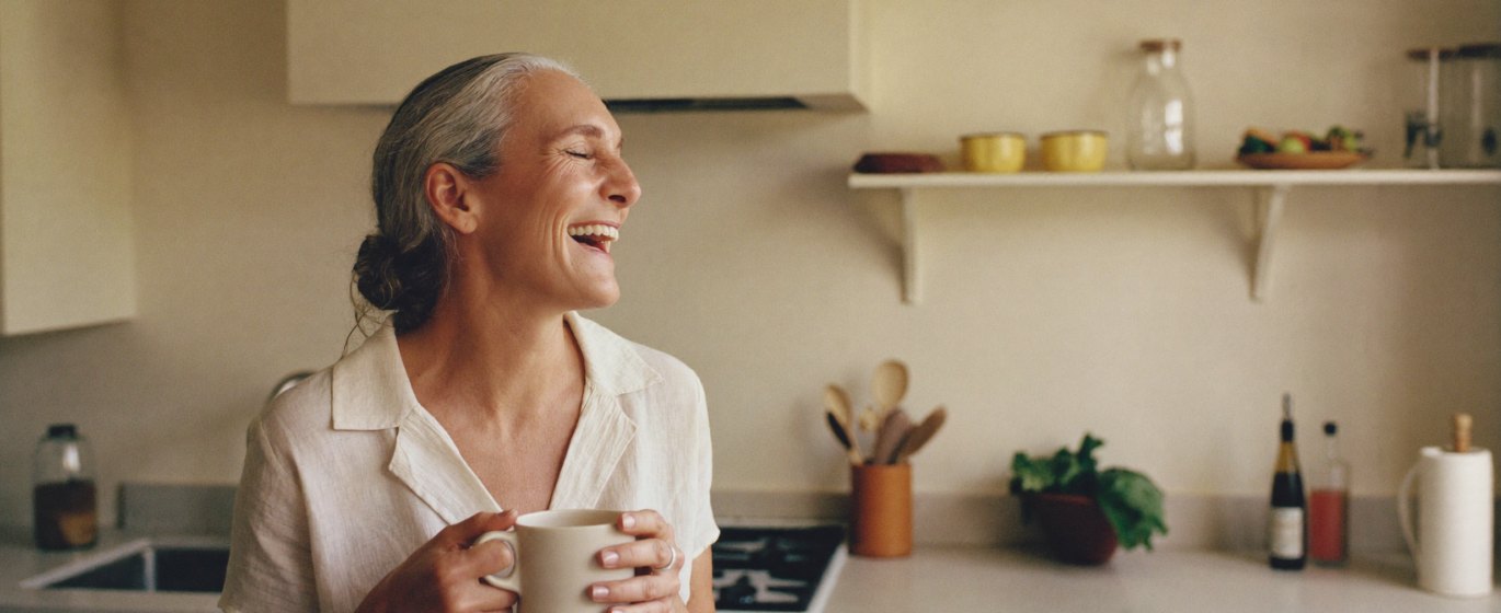 Woman laughing in her kitchen holding a mug